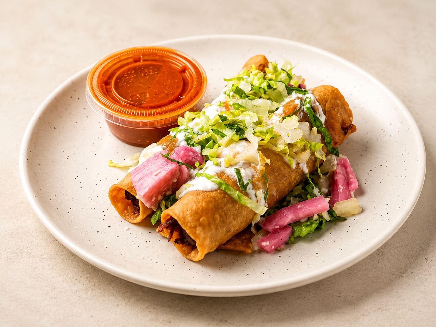 A breaded stuffed poblano pepper on a white plate under cheese sauce, topped with pico de gallo.