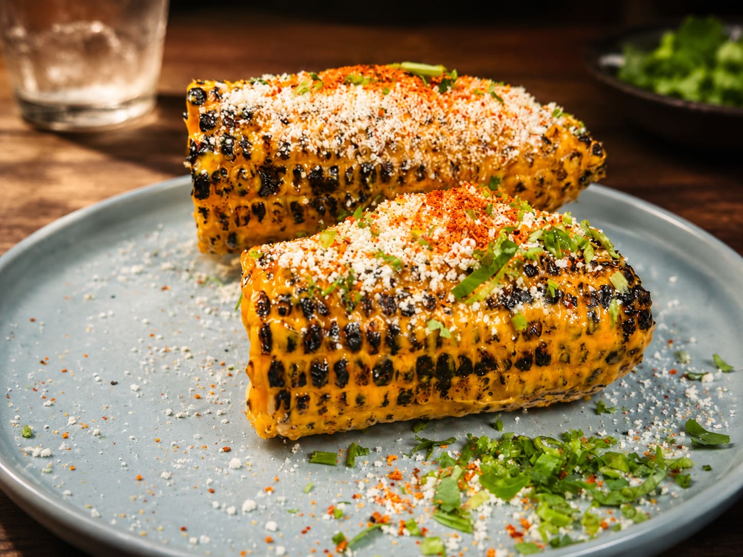 Two charred cobs of Mexican street corn dusted with Cotija, chilli and cilantro.