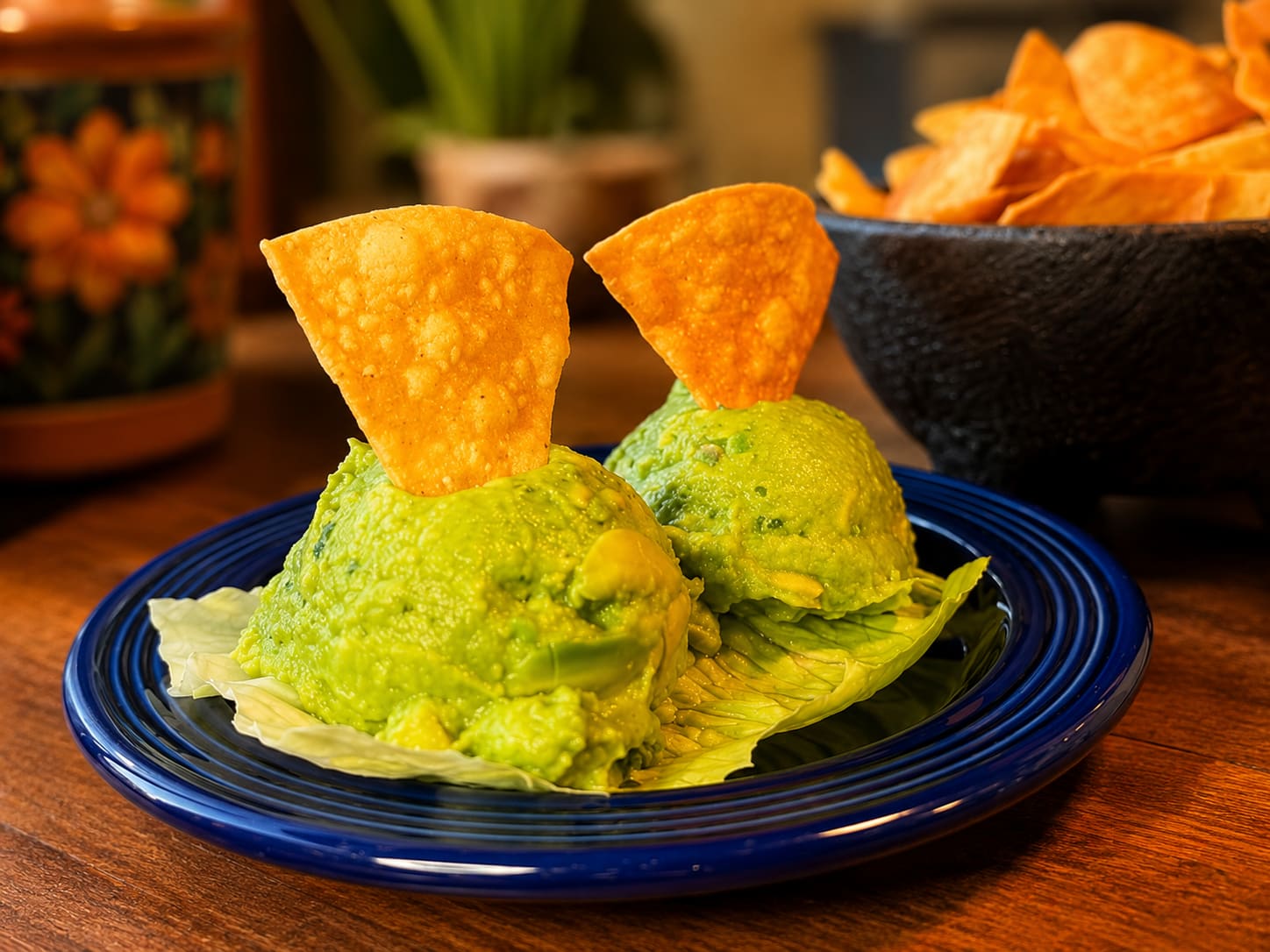 Two scoops of fresh guacamole on a blue plate with tortilla chips standing in them.