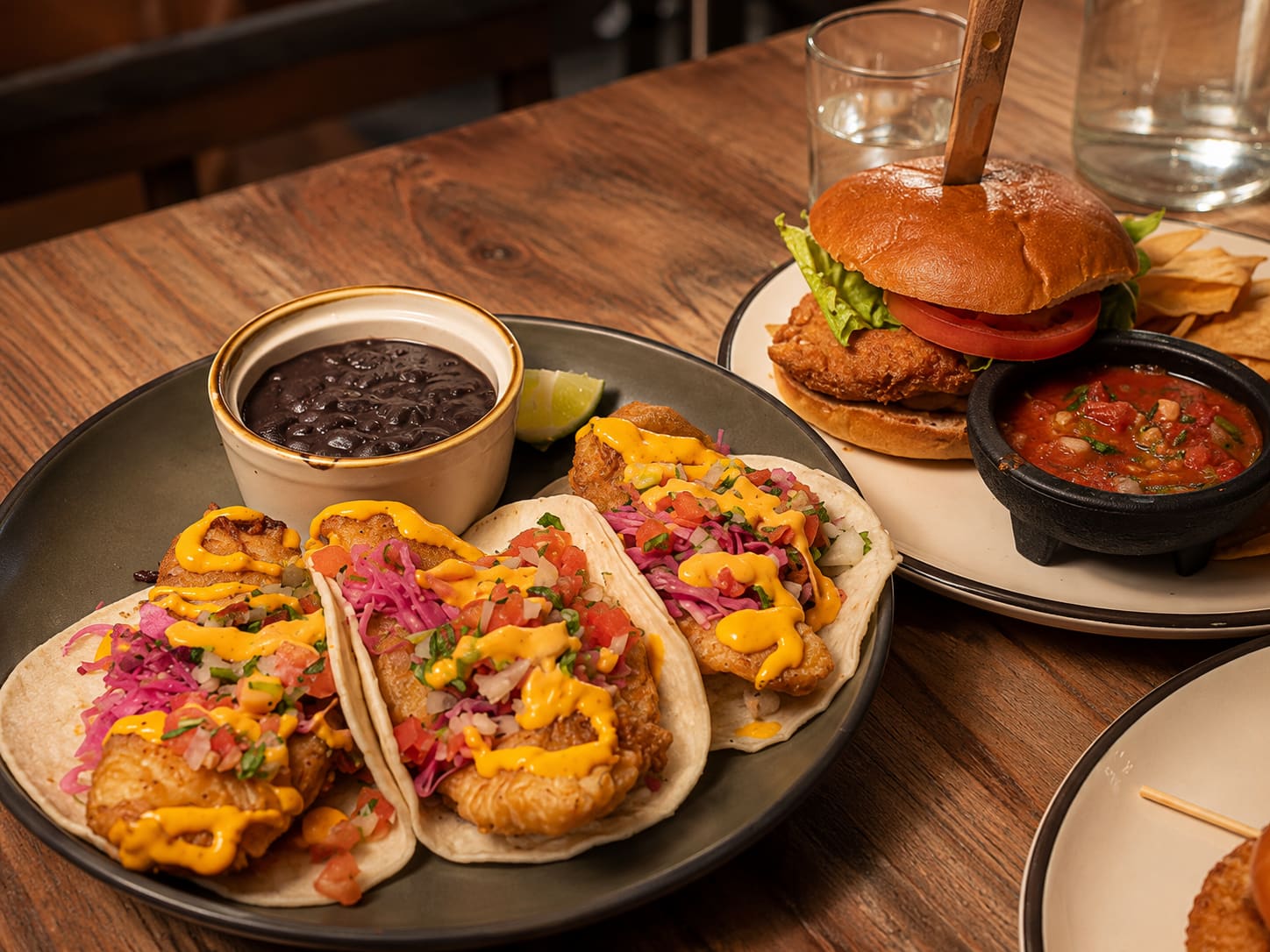 Three crispy fish tacos with chipotle sauce, pickled cabbage and pico de gallo, with a pot of black beans.